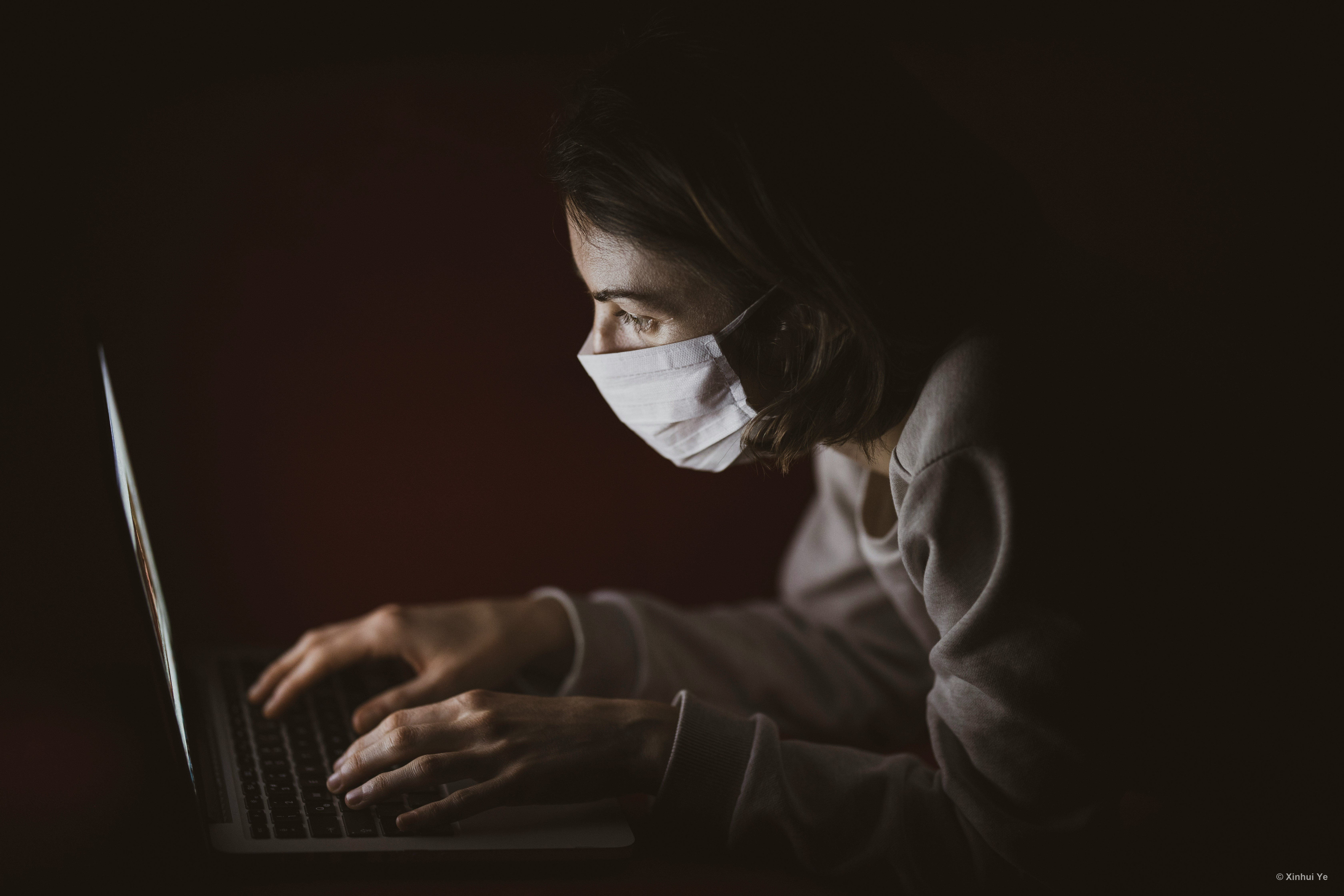 A masked person working late at a laptop